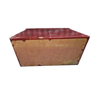 Puede incluir: Una caja roja vintage con tapa con bisagras. La caja tiene forma rectangular con un forro de papel estampado en los laterales. La caja parece ser de madera y muestra signos de desgaste.