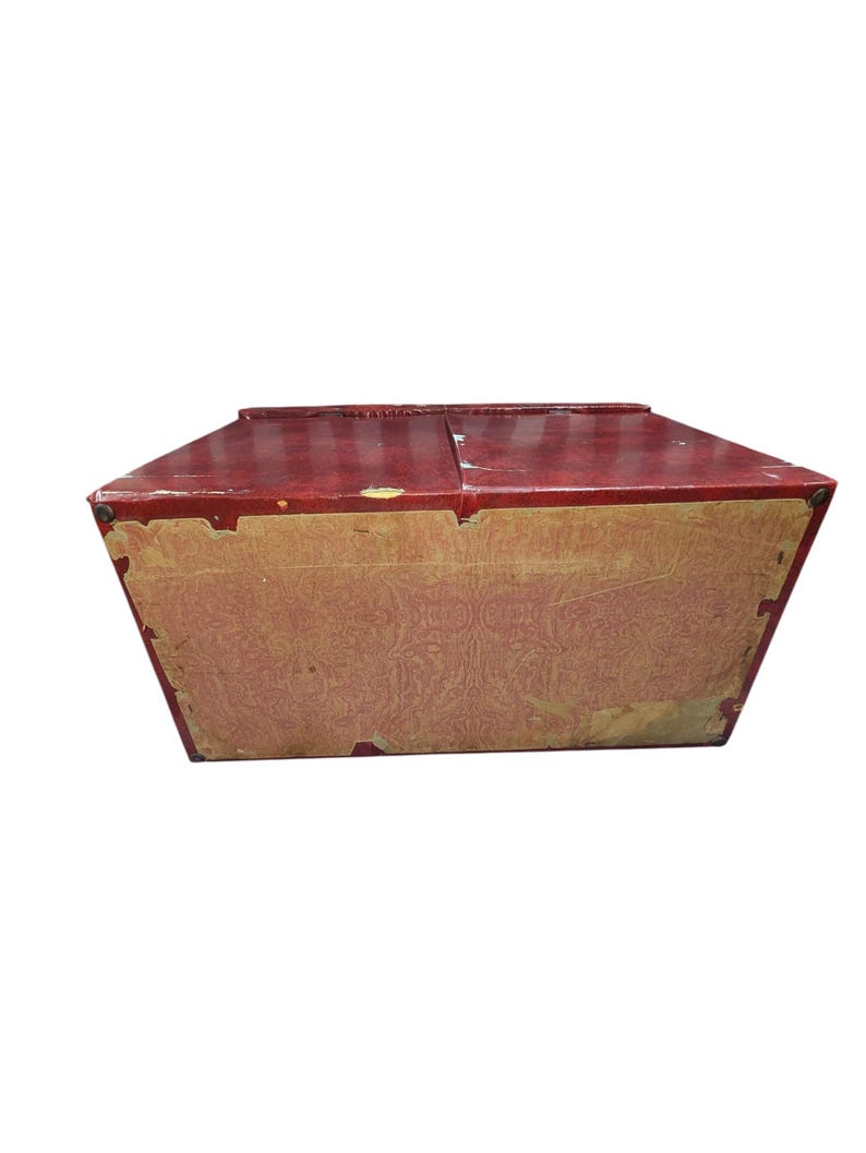 Puede incluir: Una caja roja vintage con tapa con bisagras. La caja tiene forma rectangular con un forro de papel estampado en los laterales. La caja parece ser de madera y muestra signos de desgaste.