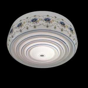 May include: A white ceramic light fixture with a floral design. The fixture has a rounded shape with blue and yellow floral patterns around the top edge. Blue stripes encircle the fixture's lower portion.