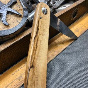 May include: A wooden-handled straight razor with a dark brown wood handle and a silver rivet. The blade is partially open and has a dark patina.