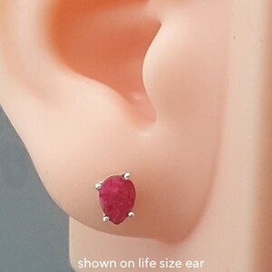 May include: A close-up of a red pear-shaped gemstone earring with silver settings. The earring is shown on a life-size ear.