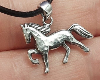 May include: A silver horse pendant necklace on a black leather cord. The horse is in a running pose with a textured finish.