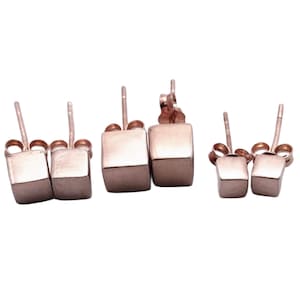 May include: A set of three pairs of rose gold cube stud earrings. The earrings are different sizes, with the smallest pair being the most delicate.