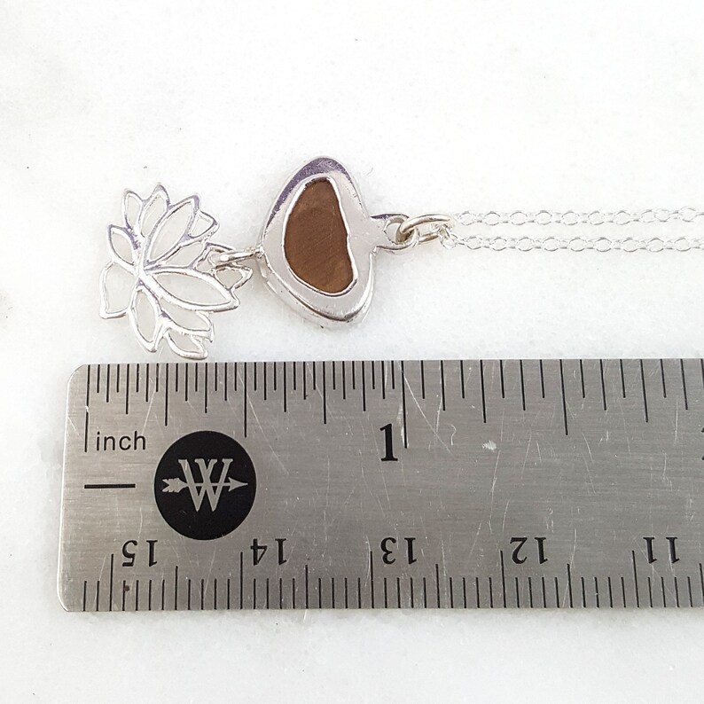 May include: Silver necklace with a brown heart-shaped pendant and a silver lotus flower charm. The necklace is measured against a ruler, showing it is just over 1 inch long.