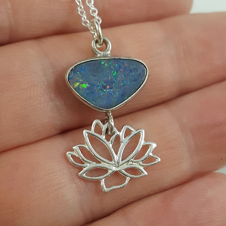 May include: A silver necklace with a blue opal pendant and a silver lotus flower charm.