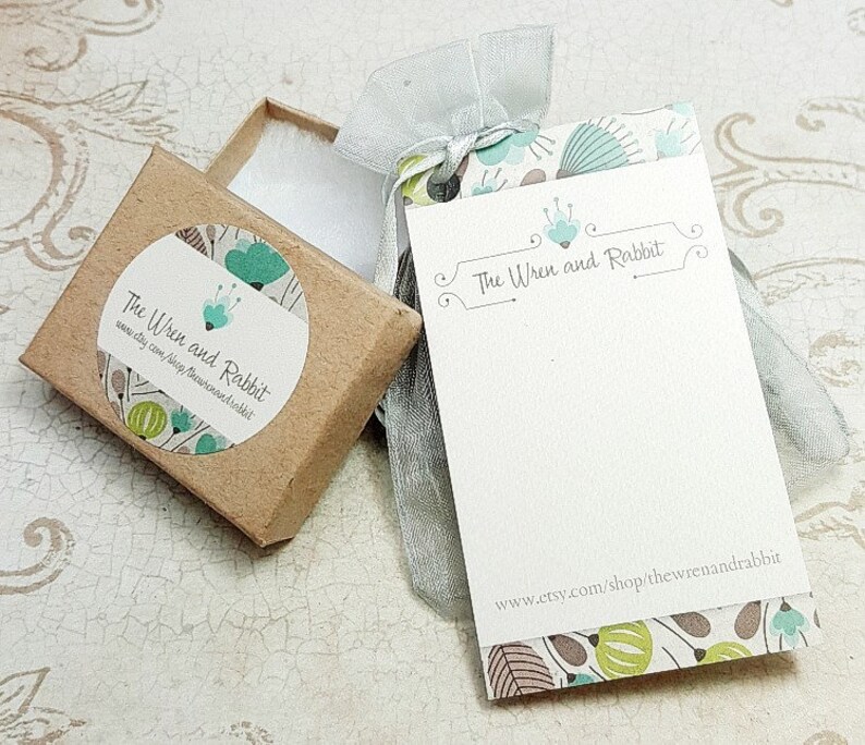May include: A small brown box with a white circle sticker that says "The Wren and Rabbit" with a green and blue floral design. The box is sitting on a white surface next to a white card with the same floral design and the text "The Wren and Rabbit" and "www.etsy.com/shop/thewrenandrabbit".