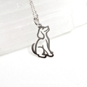 May include: Silver necklace with a cutout design of a dog sitting and looking up. The chain is delicate and the pendant is small.
