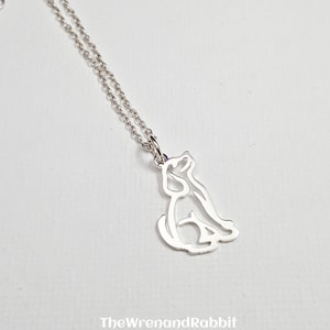 May include: A silver necklace with a delicate outline of a dog sitting. The chain is a simple silver chain.
