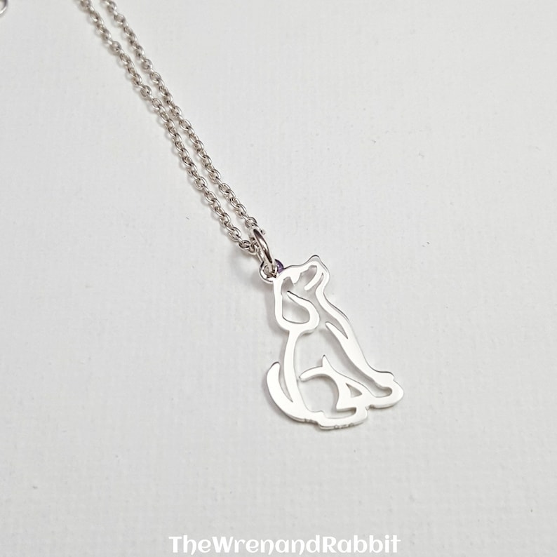 May include: A silver necklace with a delicate outline of a dog sitting. The chain is a simple silver chain.