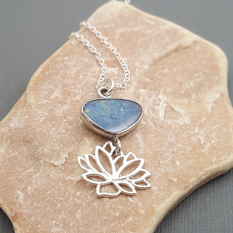 May include: A silver necklace with a blue opal pendant and a silver lotus flower charm.
