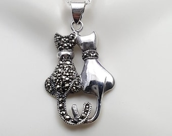 May include: A silver necklace with a pendant featuring two cats, one with a black marcasite finish and the other with a silver finish. The cats are facing each other and appear to be kissing.