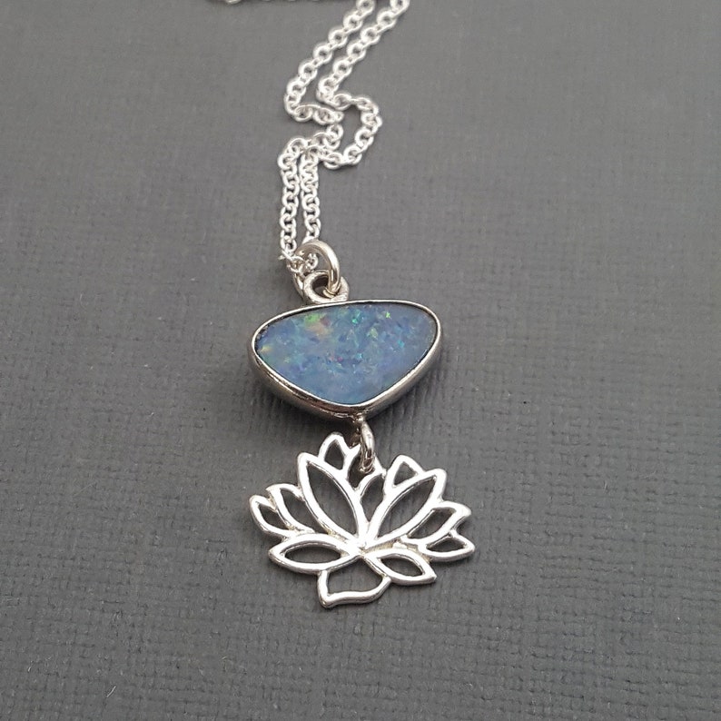 May include: A silver necklace with a blue opal pendant and a silver lotus flower charm.