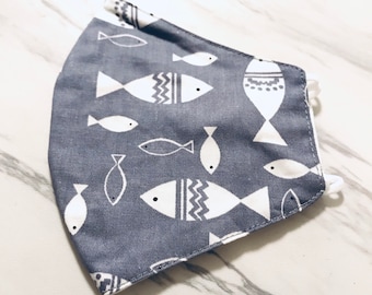 May include: A gray face mask with a white fish pattern. The fish designs vary in style, some with zigzag patterns and others with simple outlines. White elastic ear loops are attached.