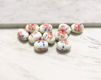 May include: A collection of white oval ceramic beads with pink and blue floral designs.