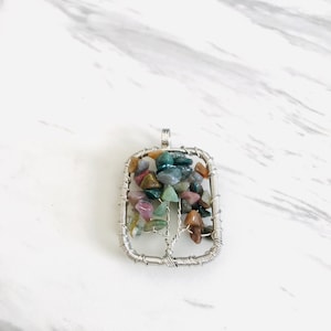 May include: A silver wire wrapped pendant featuring a tree design with various colored gemstones. The pendant is rectangular in shape and has a silver bail.