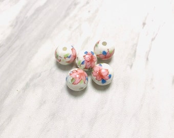 May include: Six white ceramic beads with pink and blue floral designs.