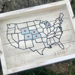 May include: A white wooden tray featuring a black outline of the United States map. The map has red hearts marking different states. The tray has two rusty metal handles.