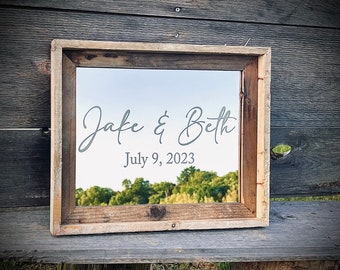May include: A rustic wooden framed mirror with a reflective surface. The mirror has a white inscription that reads "Jake & Beth July 9, 2023".