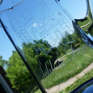 May include: A clear glass pitcher with a handle, etched with a design of a building and the text "Scholastic Dream".
