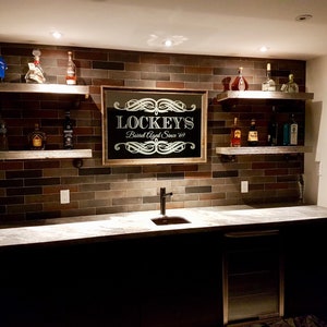 May include: A home bar with a dark wood countertop and a mirrored sign that reads "Lockey's Barrell Aged Since '69". The bar has a black faucet and a small refrigerator. There are shelves above the countertop with bottles of liquor.