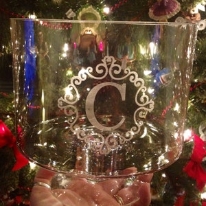 May include: A clear glass bowl with a decorative etched design featuring the letter "C" in a swirling pattern. The bowl is on a pedestal base and is perfect for serving snacks or desserts.