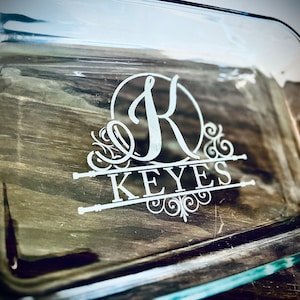 Puede incluir: Un plato para hornear de vidrio transparente con un diseño personalizado. El diseño presenta un monograma de la letra "K" en un círculo con el nombre "KEYES" debajo.