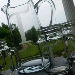 May include: A set of glass pitchers and mason jars with a frosted letter T etched on each. The jars have handles and are perfect for serving beverages.