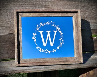 May include: A wooden framed mirror with a blue background and a white wreath with the letter "W" in the center.