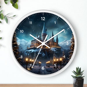Puede incluir: Reloj blanco con una imagen en blanco y negro del castillo de Hogwarts en un paisaje nevado. La esfera del reloj tiene números romanos negros y manecillas negras.