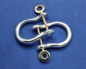 May include: A silver-colored shackle with a gold-colored pin and two eyelets. The shackle is made of metal and has a curved, U-shaped design. The pin is threaded through the shackle, securing the two sides together. The background is a solid blue.
