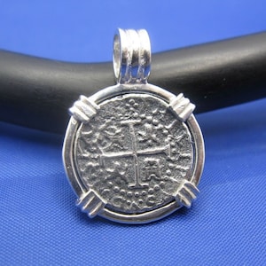 May include: Silver pendant in the shape of a coin with a cross design. The pendant has a textured surface and a silver bail.