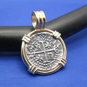 May include: Silver coin pendant with a cross design, framed in gold, on a blue background.