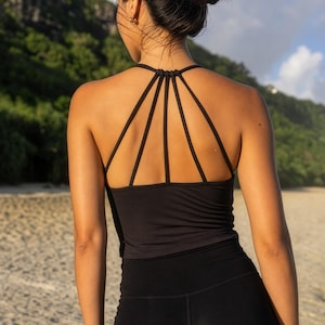 May include: A black vest top featuring a racerback design with five thin, vertical straps that connect to a central knot at the neckline. The garment is paired with matching black athletic shorts, creating a coordinated set with a clean, solid finish.