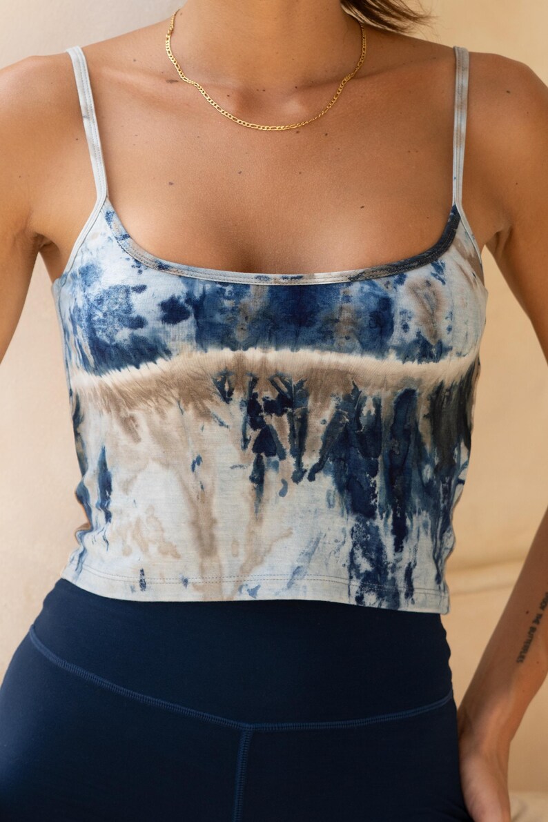 Puede incluir: Camiseta sin mangas te&ntilde;ida con tintes en tonos azules y marrones. La camiseta tiene tirantes finos y un escote redondo. El modelo tambi&eacute;n lleva leggings azul marino y un collar de cadena dorada. El estilo general es informal y c&oacute;modo.
