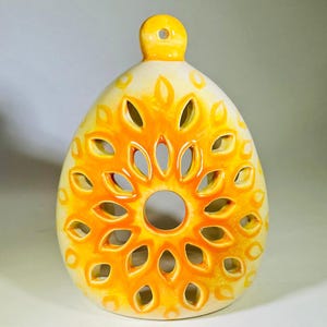 Peut inclure: Un bougeoir en céramique jaune et blanc avec un motif découpé. Le bougeoir est en forme de larme et possède une petite boucle en haut pour l'accrocher.