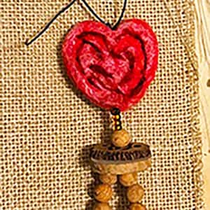 May include: A handcrafted necklace with a red heart pendant, wooden beads, a black bead, and a wooden peace symbol. The necklace is suspended on a black cord against a burlap backdrop.