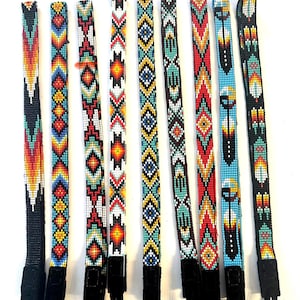 May include: Nine long, narrow camera straps arranged vertically, each featuring intricate, multi-colored glass beadwork in geometric patterns. Each strap is numbered #1 through #9 and includes black leather ends with thin black attachment cords.