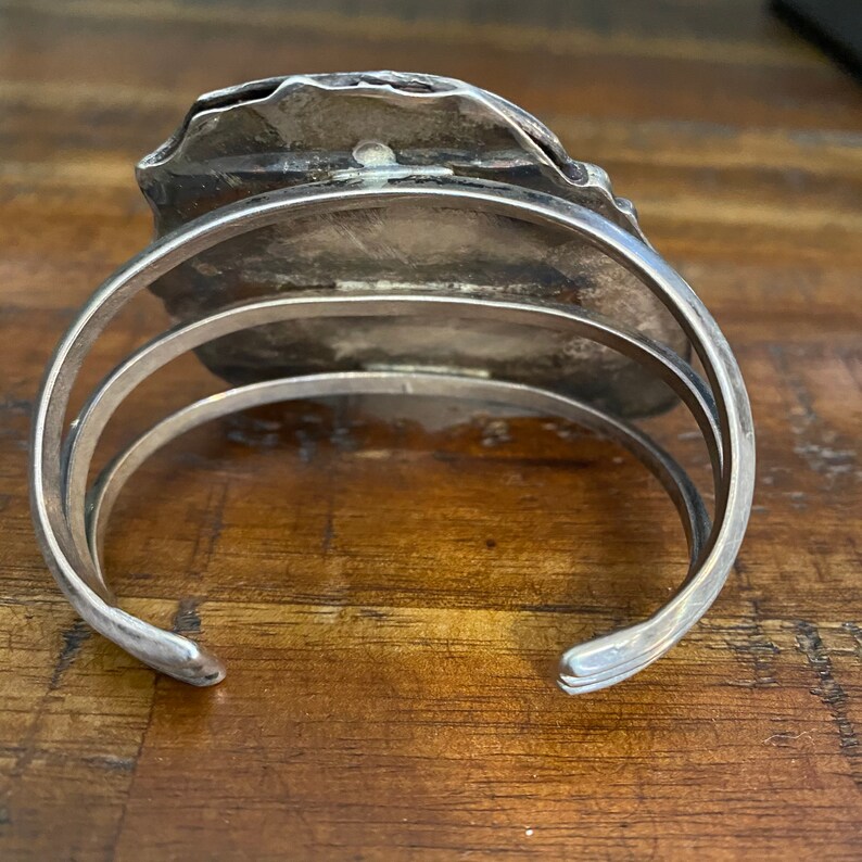 May include: Silver cuff bracelet with a textured, irregular shaped design. The bracelet is open and has a hinged closure.