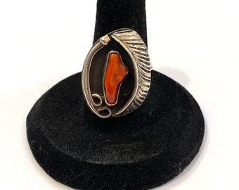 May include: A silver ring with a coral stone set in a black and silver design. The ring is on a black velvet ring holder.