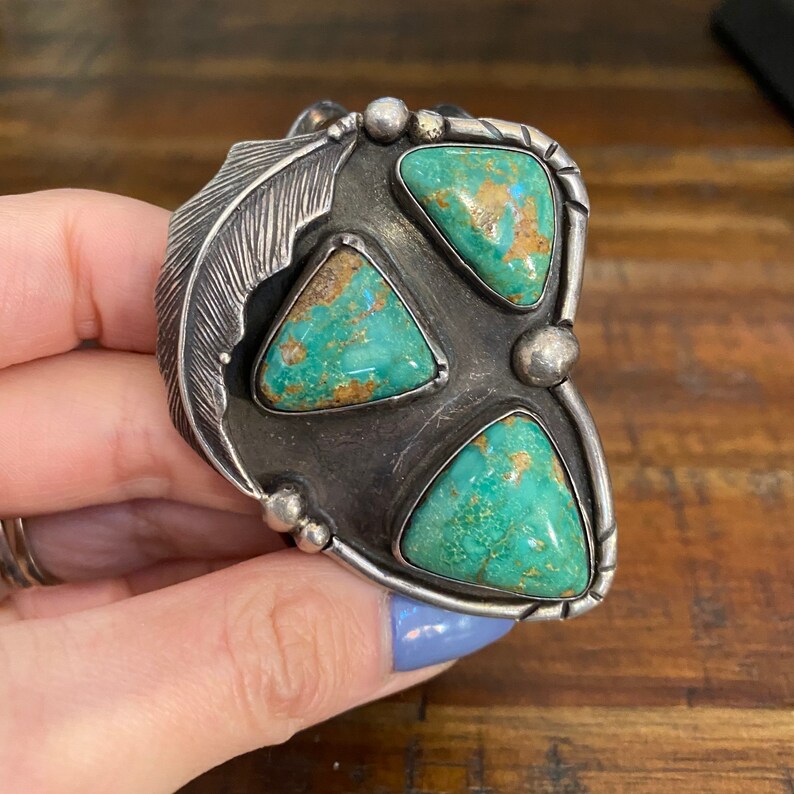 May include: A silver bracelet with a feather design and three turquoise stones set in a triangular shape.