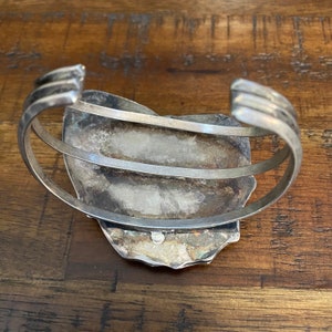 May include: Silver cuff bracelet with a large, oval-shaped turquoise stone set in the center. The bracelet is made of two bands of silver that wrap around the wrist.