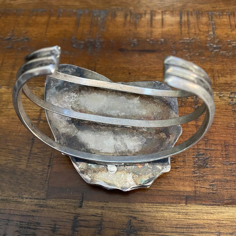 May include: Silver cuff bracelet with a large, oval-shaped turquoise stone set in the center. The bracelet is made of two bands of silver that wrap around the wrist.