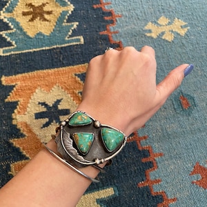 May include: A silver bracelet with a turquoise stone design. The bracelet is worn on a person's wrist.