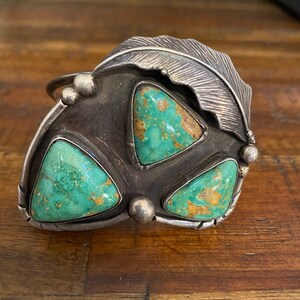 May include: A silver bracelet with a turquoise stone design. The bracelet features three triangular turquoise stones set in a silver frame with a feather design.