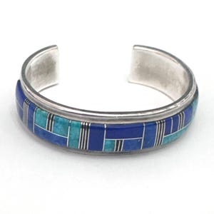 May include: A silver cuff bracelet with a geometric pattern of blue turquoise and lapis lazuli stones.