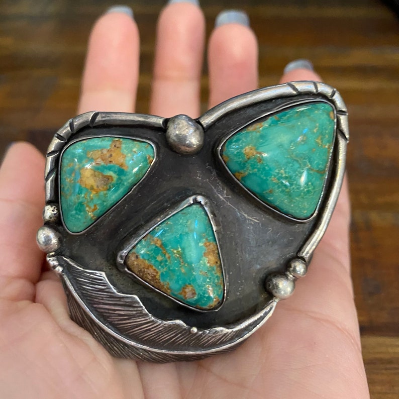 May include: A silver and turquoise Native American style ring with three triangular turquoise stones set in a silver feather design.