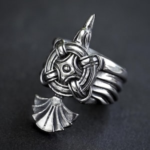 Op de afbeelding: Een zilveren ring met een gedetailleerd ontwerp met een vogel met uitgespreide vleugels en een cirkelvormig knoopwerkpatroon.