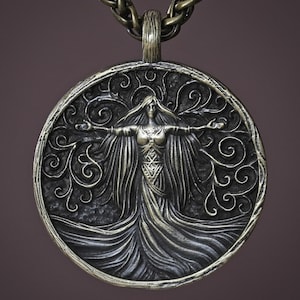 May include: A silver-toned pendant necklace featuring a detailed circular design. The pendant depicts a woman with outstretched arms, surrounded by swirling patterns. The necklace has a textured chain and a dark background.