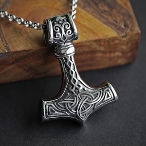 Könnte beinhalten: Eine silberne Mjolnir-Halskette mit komplizierten Knotenmustern. Der Anhänger ist an einer silbernen Kette.