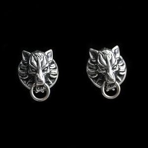 May include: A pair of silver wolf head earrings with a ring detail. The earrings are on a black background.